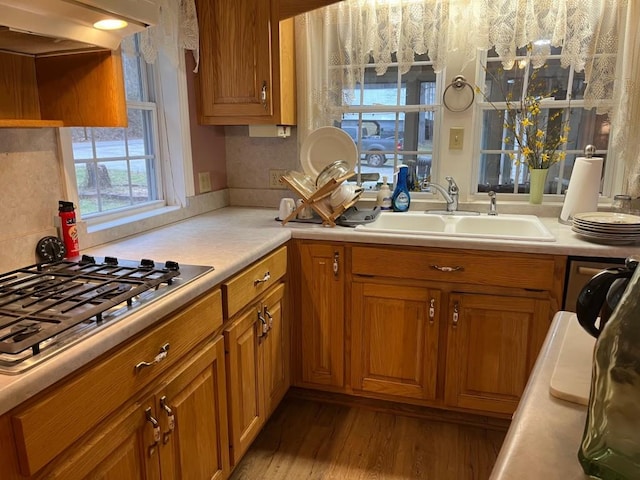 kitchen featuring a sink, light countertops, stainless steel gas stovetop, under cabinet range hood, and brown cabinets