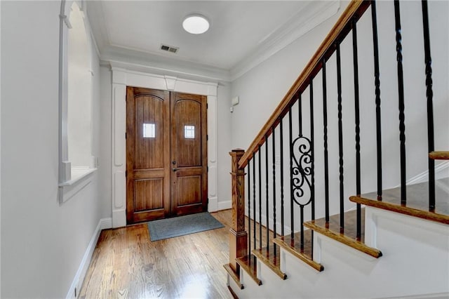 foyer entrance with ornamental molding, visible vents, baseboards, and hardwood / wood-style flooring