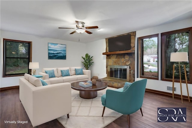 living room featuring hardwood / wood-style floors, ceiling fan, and a stone fireplace