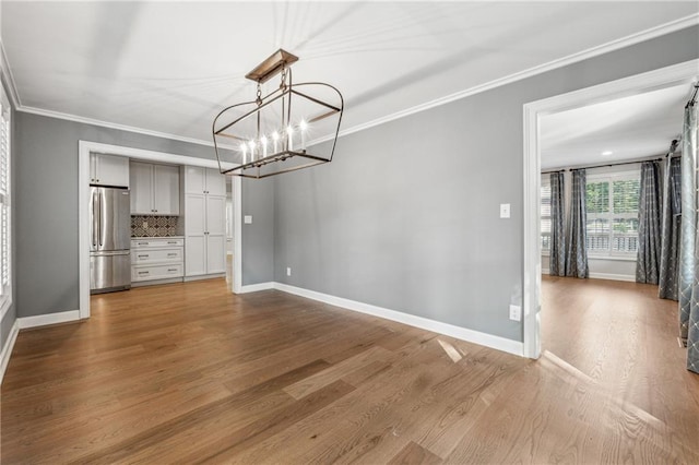 unfurnished dining area featuring ornamental molding, a notable chandelier, and light hardwood / wood-style floors