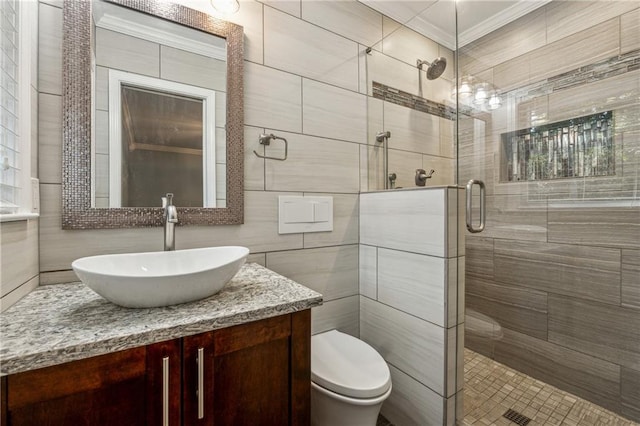 bathroom with a shower with door, toilet, tile walls, vanity, and crown molding