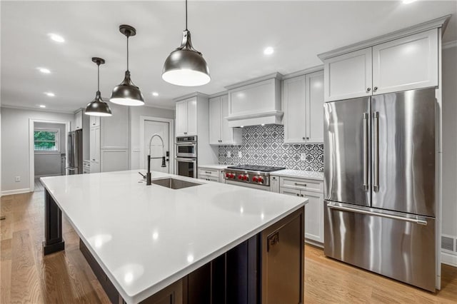 kitchen featuring light wood-type flooring, a large island, stainless steel appliances, decorative light fixtures, and custom exhaust hood