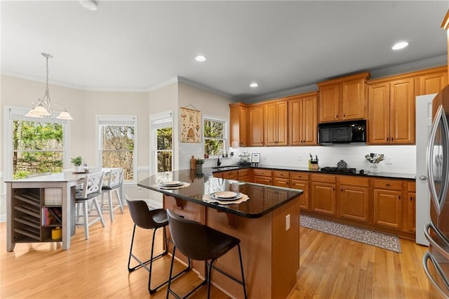 kitchen featuring light wood-type flooring, black appliances, a breakfast bar, a sink, and tasteful backsplash