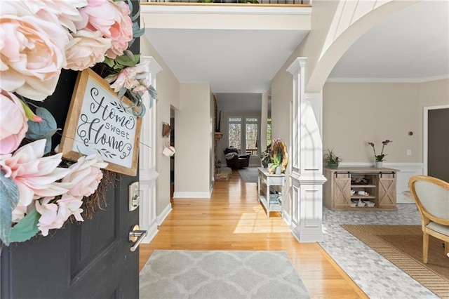 foyer featuring a wainscoted wall, ornamental molding, wood finished floors, arched walkways, and decorative columns