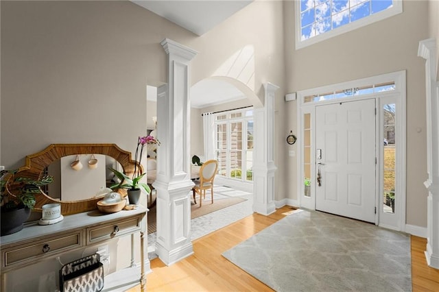 entrance foyer with light wood-type flooring, baseboards, a towering ceiling, and ornate columns