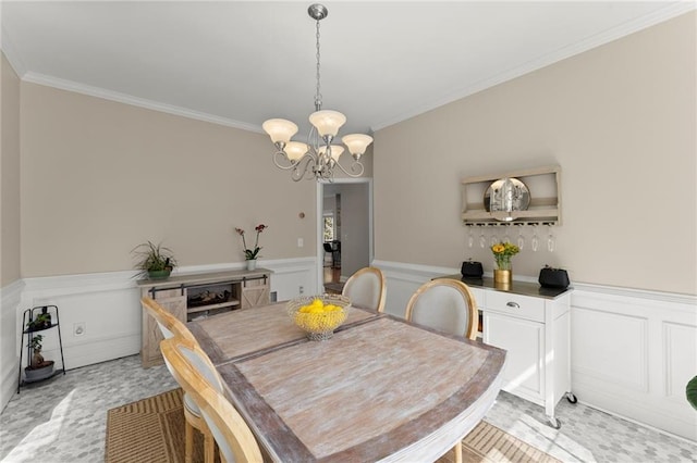 dining room with a decorative wall, wainscoting, crown molding, and an inviting chandelier