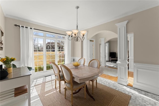 dining space featuring arched walkways, wainscoting, ornamental molding, and decorative columns