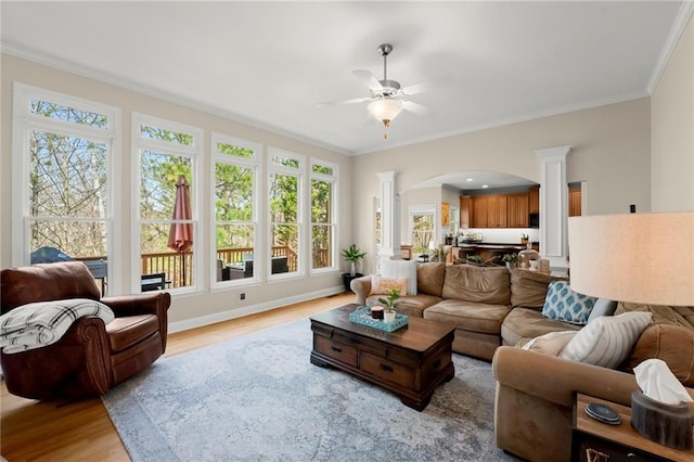 living room featuring light wood-type flooring, arched walkways, ceiling fan, and crown molding