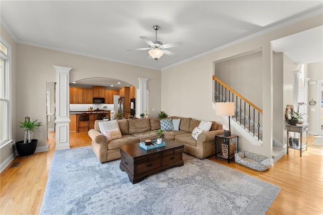 living area with light wood-type flooring, ornamental molding, plenty of natural light, stairway, and ornate columns