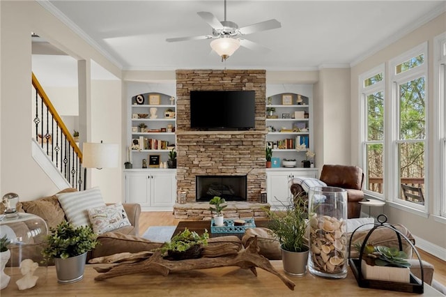 living room featuring built in features, wood finished floors, ornamental molding, a stone fireplace, and stairs