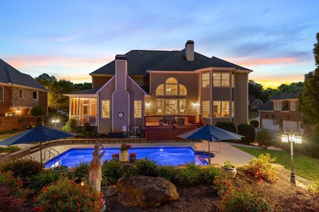 2439 Huntington Park Dr NW, Acworth, GA 30101 - back of house at dusk featuring a chimney, an outdoor pool, a patio area, and a wooden deck