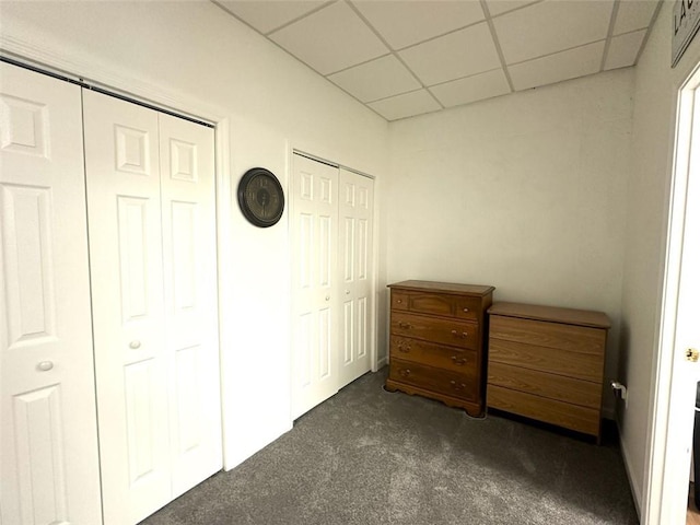 unfurnished bedroom featuring a drop ceiling, two closets, and dark colored carpet