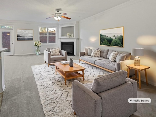 living room featuring baseboards, a ceiling fan, light colored carpet, a fireplace with flush hearth, and crown molding