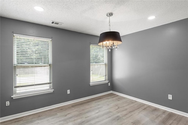 empty room featuring wood-type flooring, a textured ceiling, plenty of natural light, and an inviting chandelier