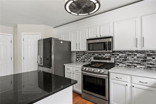 kitchen with appliances with stainless steel finishes, white cabinets, dark stone counters, and light hardwood / wood-style floors