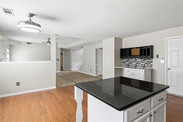 kitchen featuring light hardwood / wood-style flooring, a center island, white cabinetry, a textured ceiling, and tasteful backsplash