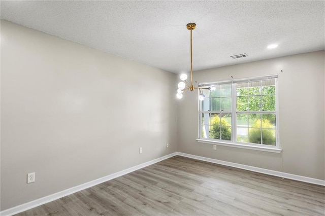 empty room featuring an inviting chandelier, a textured ceiling, and hardwood / wood-style flooring