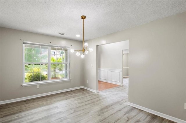 unfurnished dining area with a notable chandelier, a textured ceiling, and light wood-type flooring