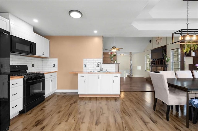 kitchen featuring black appliances, a sink, open floor plan, butcher block countertops, and white cabinets