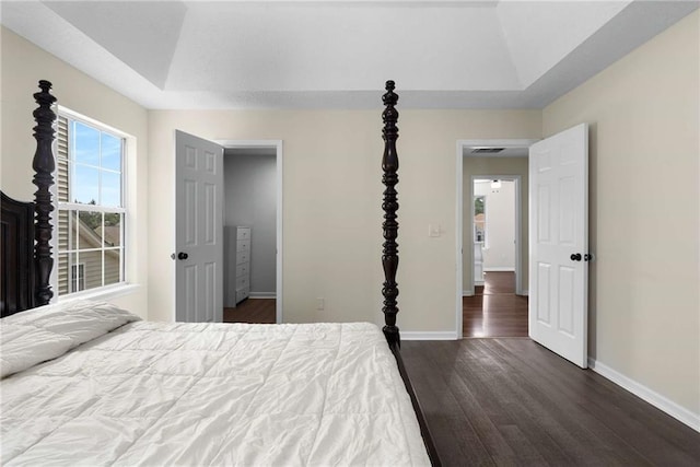 bedroom with dark wood-style flooring, baseboards, and a raised ceiling