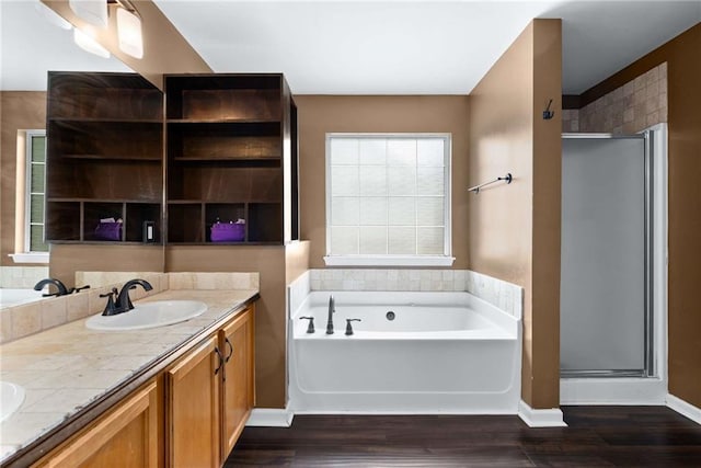 bathroom featuring double vanity, a shower stall, a bath, and wood finished floors