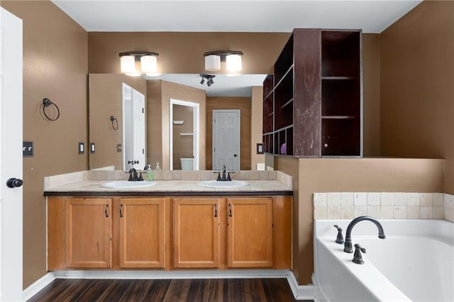 bathroom with a bath, wood finished floors, double vanity, and baseboards