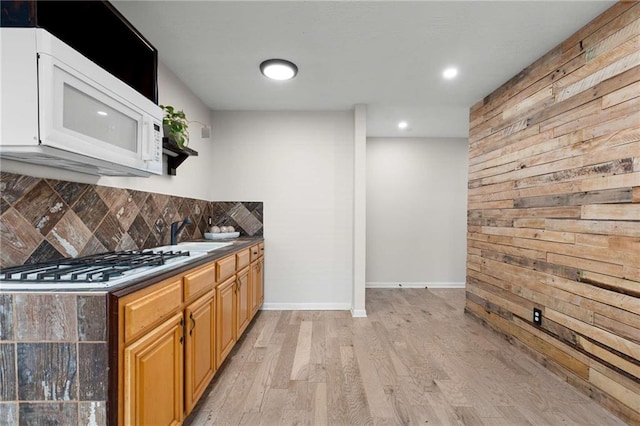 kitchen with white microwave, stainless steel gas stovetop, wood walls, decorative backsplash, and light wood finished floors