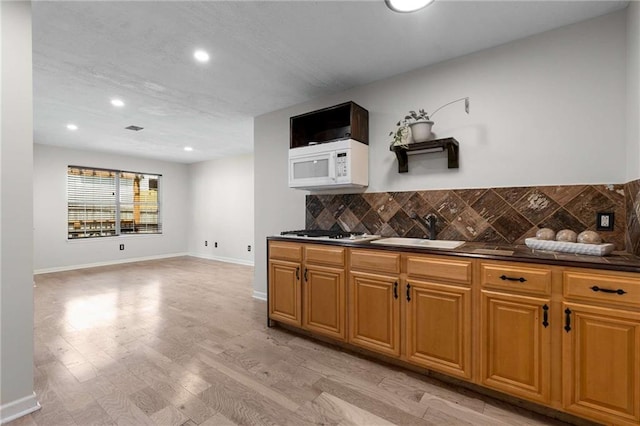 kitchen with a sink, white microwave, dark countertops, gas stovetop, and decorative backsplash