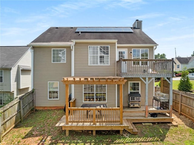 back of house featuring a wooden deck, a chimney, a fenced backyard, and roof mounted solar panels