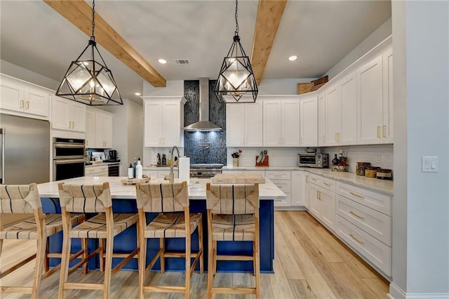 132 Swift Creek Way, Jefferson, GA 30549 - kitchen with white cabinets, a kitchen island with sink, wall chimney range hood, beamed ceiling, and hanging light fixtures