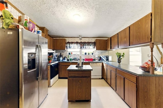 kitchen with stainless steel appliances, dark countertops, a kitchen island, a peninsula, and under cabinet range hood