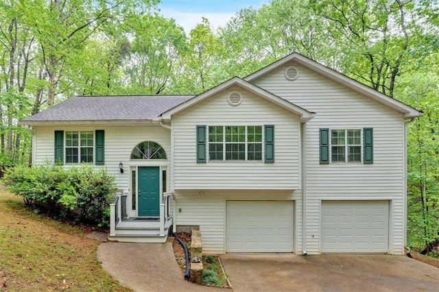 raised ranch featuring an attached garage, a shingled roof, and concrete driveway