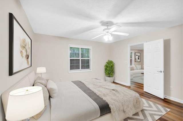 bedroom featuring baseboards, ceiling fan, a textured ceiling, and wood finished floors