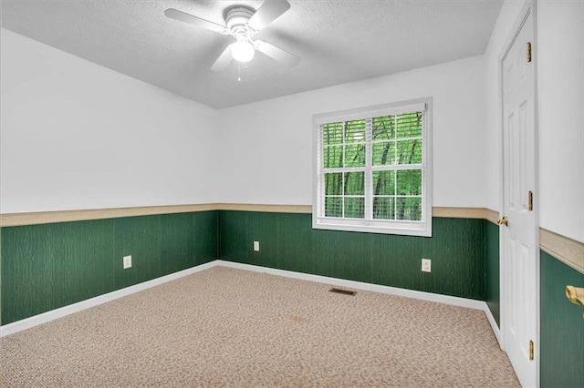 unfurnished room with a wainscoted wall, a textured ceiling, carpet floors, and visible vents