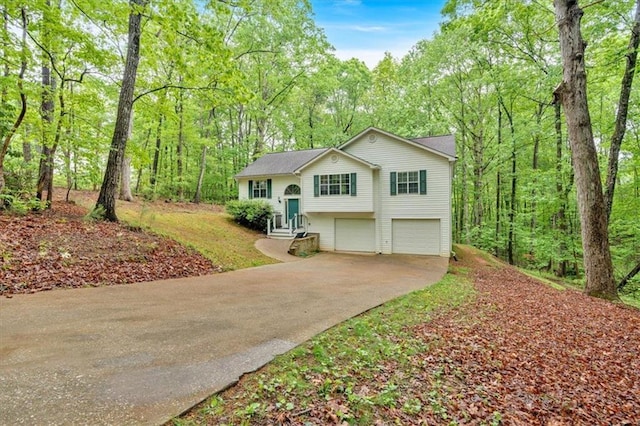 bi-level home with a garage, a forest view, and concrete driveway