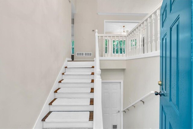 stairway with baseboards, visible vents, and a towering ceiling
