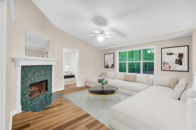 living area with wood finished floors, baseboards, a tile fireplace, a ceiling fan, and vaulted ceiling