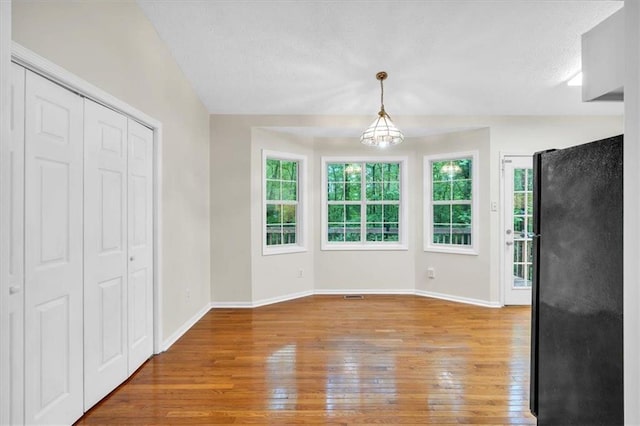 unfurnished dining area featuring light wood-style floors, baseboards, and a notable chandelier