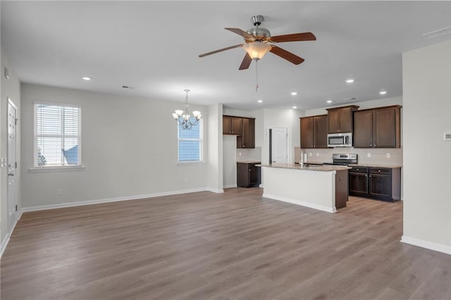 kitchen with appliances with stainless steel finishes, ceiling fan with notable chandelier, a kitchen island with sink, pendant lighting, and wood-type flooring