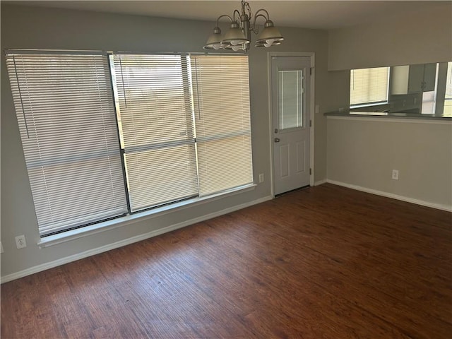 unfurnished room featuring an inviting chandelier, baseboards, and wood finished floors