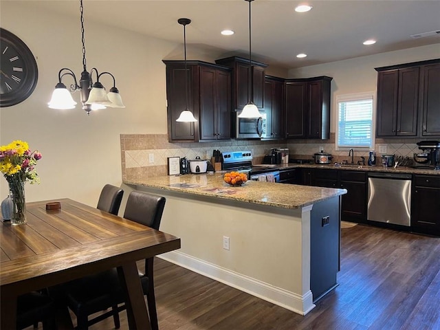 kitchen with dark brown cabinetry, appliances with stainless steel finishes, hanging light fixtures, a peninsula, and light stone countertops