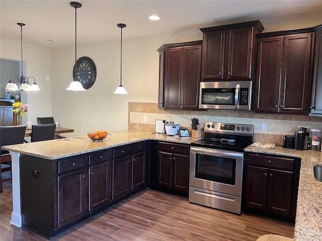 kitchen featuring a peninsula, appliances with stainless steel finishes, wood finished floors, and decorative light fixtures