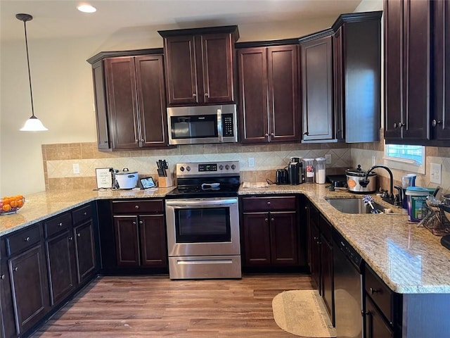 kitchen featuring appliances with stainless steel finishes, decorative light fixtures, dark brown cabinets, light wood-style floors, and a sink