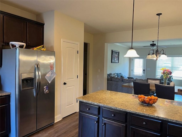 kitchen with light stone counters, dark wood-style flooring, decorative light fixtures, open floor plan, and stainless steel fridge