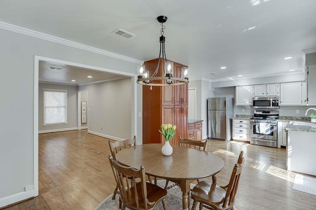dining room featuring an inviting chandelier, ornamental molding, baseboards, light wood finished floors, and visible vents