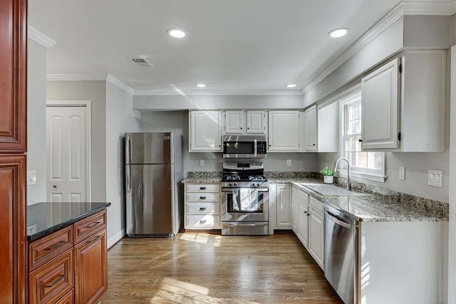 kitchen featuring visible vents, ornamental molding, wood finished floors, stainless steel appliances, and a sink