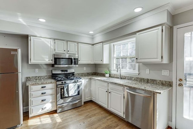 kitchen with white cabinetry, ornamental molding, stainless steel appliances, a sink, and light wood-style flooring