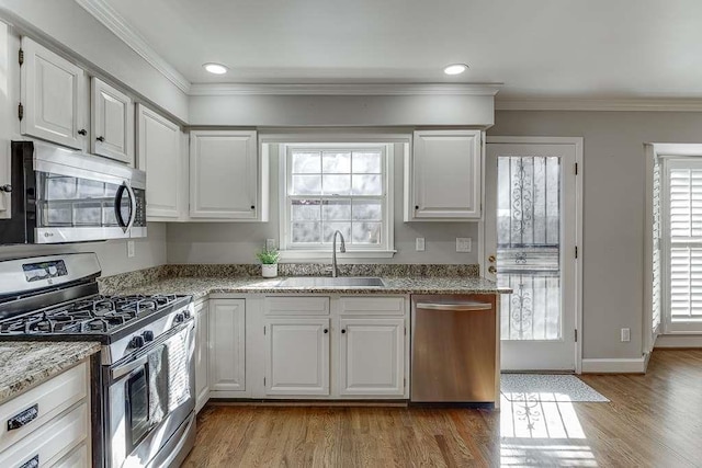 kitchen featuring ornamental molding, wood finished floors, stainless steel appliances, white cabinetry, and a sink