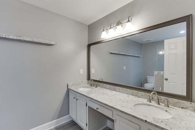full bath with toilet, a sink, double vanity, and baseboards