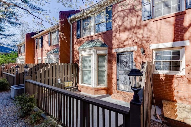 view of exterior entry featuring brick siding, central AC, and fence
